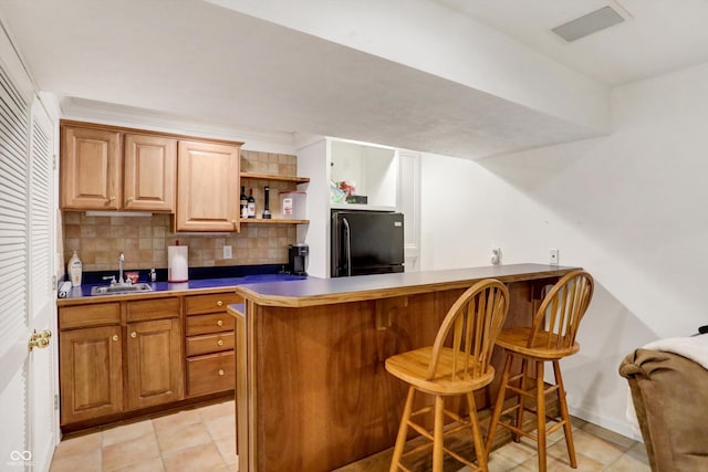 kitchen with sink, a breakfast bar area, black refrigerator, kitchen peninsula, and decorative backsplash