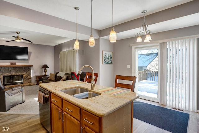 kitchen with sink, dishwasher, a kitchen island with sink, light stone counters, and decorative light fixtures