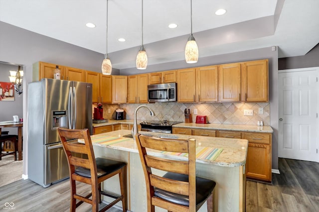 kitchen with stainless steel appliances, light stone countertops, a center island with sink, dark hardwood / wood-style flooring, and decorative light fixtures