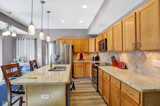 kitchen featuring sink, appliances with stainless steel finishes, a kitchen breakfast bar, an island with sink, and pendant lighting