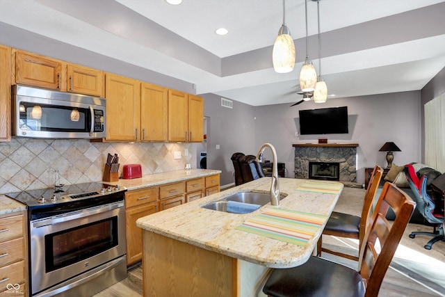 kitchen featuring sink, a breakfast bar area, appliances with stainless steel finishes, light stone countertops, and a center island with sink