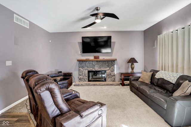 carpeted living room with a stone fireplace and ceiling fan