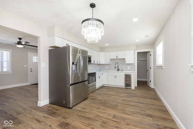 kitchen with white cabinetry, stainless steel appliances, wine cooler, decorative backsplash, and ceiling fan with notable chandelier