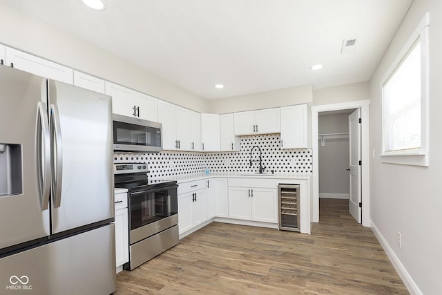 kitchen with stainless steel appliances, beverage cooler, sink, white cabinets, and hardwood / wood-style floors