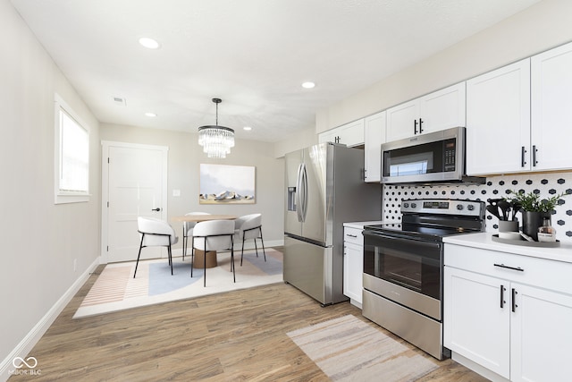 kitchen featuring backsplash, white cabinets, decorative light fixtures, and appliances with stainless steel finishes