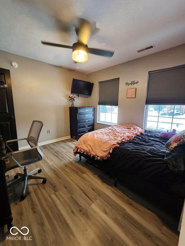 bedroom with ceiling fan, wood-type flooring, and multiple windows