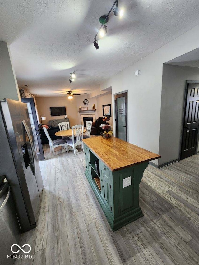 kitchen with wood counters, stainless steel refrigerator with ice dispenser, a textured ceiling, green cabinetry, and a kitchen island