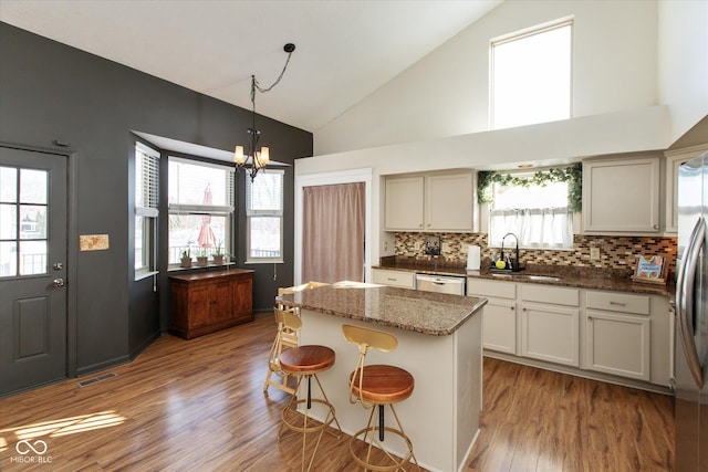 kitchen with dishwasher, a breakfast bar, a kitchen island, high vaulted ceiling, and dark stone counters