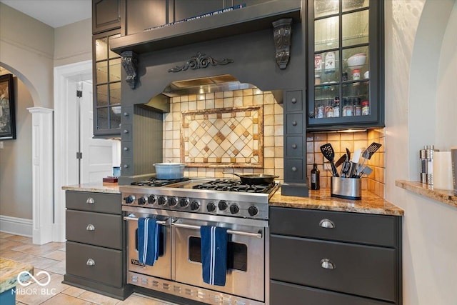 kitchen featuring light stone countertops, range hood, double oven range, and decorative backsplash