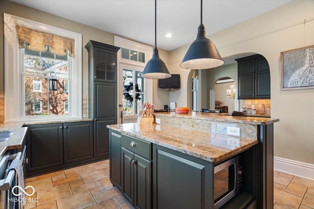 kitchen with light stone countertops, dishwasher, decorative light fixtures, tasteful backsplash, and a kitchen island