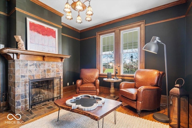 sitting room featuring a notable chandelier, a tiled fireplace, crown molding, and hardwood / wood-style flooring