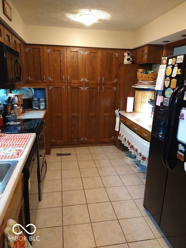 kitchen with light tile patterned floors, black appliances, and a textured ceiling