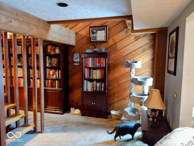 sitting room featuring beam ceiling, wooden walls, carpet floors, and a textured ceiling