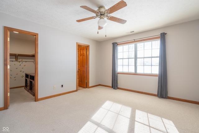 unfurnished bedroom with a textured ceiling, ceiling fan, a closet, a walk in closet, and light colored carpet