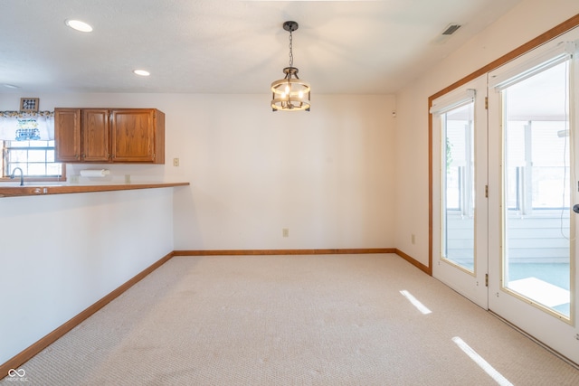 unfurnished dining area featuring sink, an inviting chandelier, and light carpet