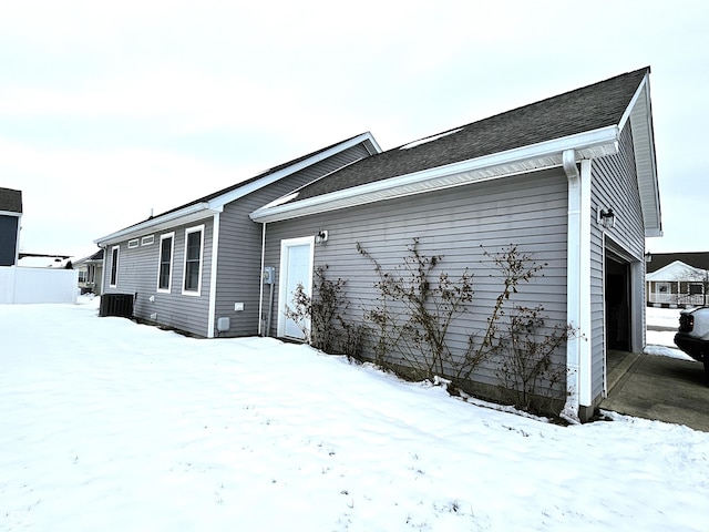 view of snow covered exterior with central AC unit and a garage