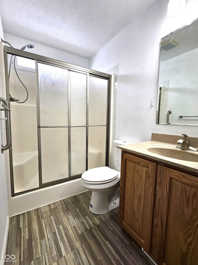 bathroom featuring hardwood / wood-style floors, toilet, vanity, a shower with door, and a textured ceiling