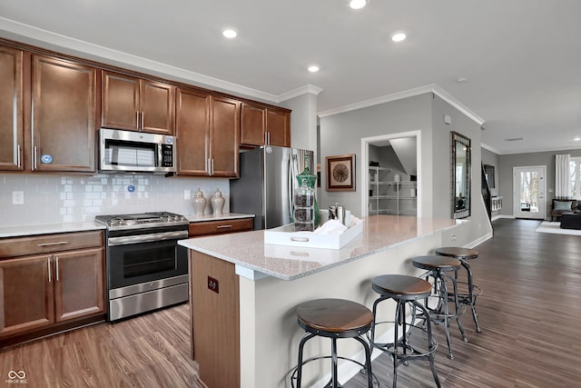 kitchen with a breakfast bar area, stainless steel appliances, wood finished floors, backsplash, and a center island