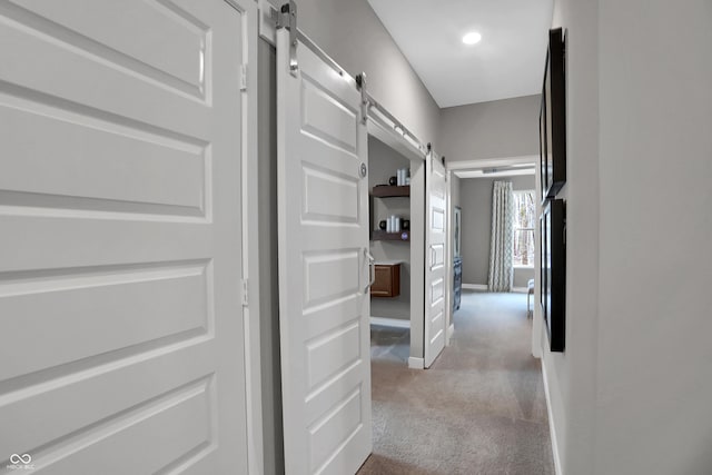 hall with a barn door, carpet, and baseboards