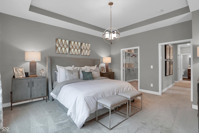 carpeted bedroom with a walk in closet, baseboards, and a raised ceiling