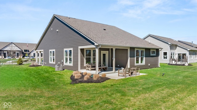 rear view of property featuring a yard, a shingled roof, and a patio