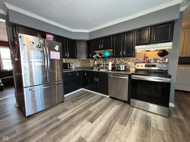 kitchen with appliances with stainless steel finishes, crown molding, light hardwood / wood-style flooring, and backsplash