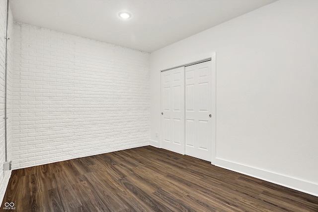 unfurnished bedroom featuring brick wall, dark hardwood / wood-style flooring, and a closet