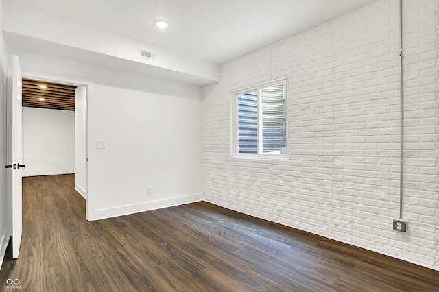 spare room featuring brick wall and dark hardwood / wood-style flooring