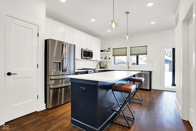 kitchen with hanging light fixtures, a kitchen bar, a kitchen island, white cabinetry, and appliances with stainless steel finishes