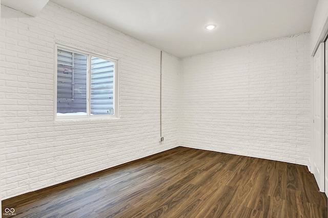 empty room featuring brick wall and dark hardwood / wood-style flooring