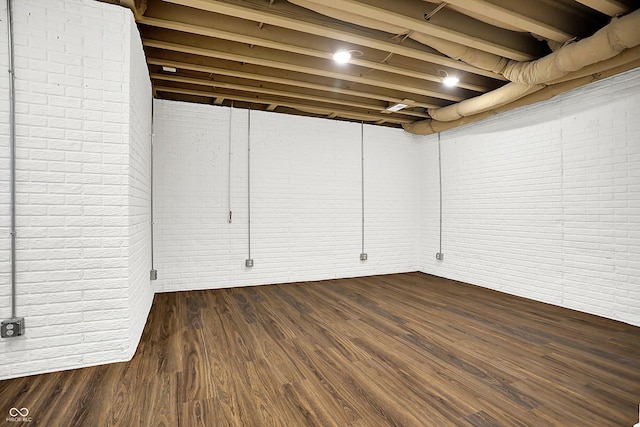 basement with brick wall and dark hardwood / wood-style flooring