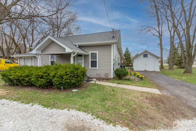 bungalow-style house featuring a front lawn, driveway, a shingled roof, and an outdoor structure