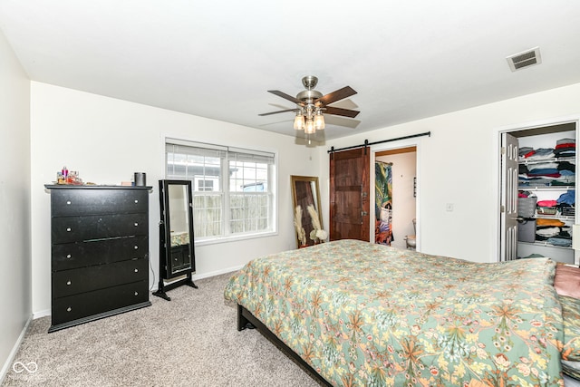 bedroom with a spacious closet, light carpet, a closet, ceiling fan, and a barn door