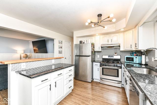 kitchen with appliances with stainless steel finishes, tasteful backsplash, a notable chandelier, white cabinets, and sink