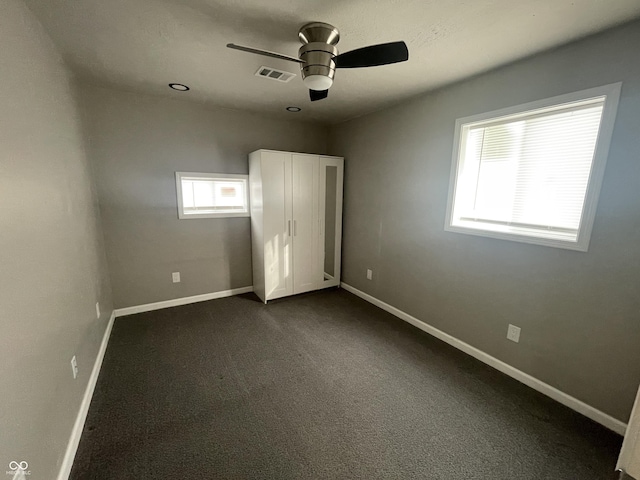 unfurnished bedroom with ceiling fan and dark colored carpet