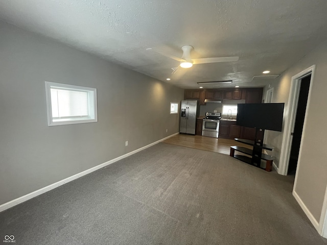 unfurnished living room with a textured ceiling, dark carpet, ceiling fan, and sink