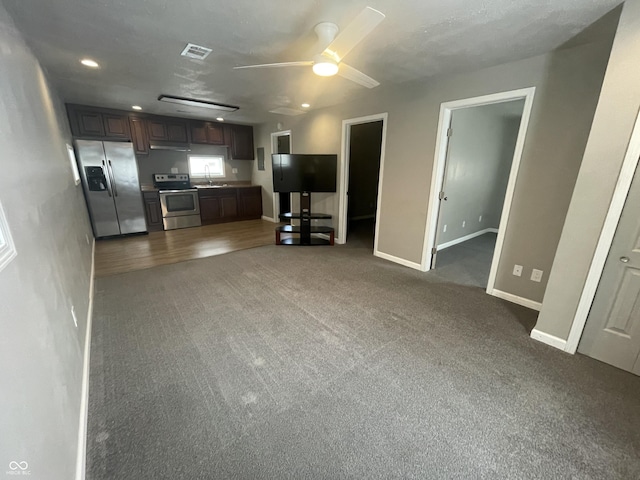 unfurnished living room with dark colored carpet, ceiling fan, and sink