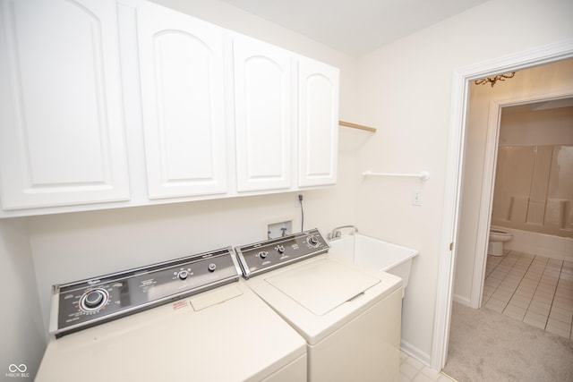 clothes washing area featuring sink, cabinets, light tile patterned flooring, and washing machine and clothes dryer