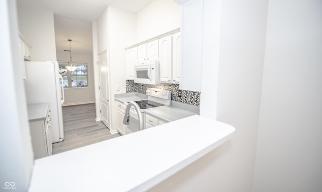 kitchen with white appliances, white cabinets, kitchen peninsula, and a chandelier