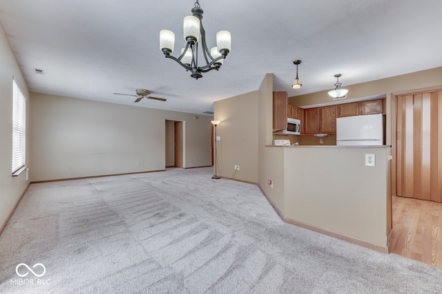 kitchen with hanging light fixtures, light carpet, white refrigerator, kitchen peninsula, and ceiling fan with notable chandelier