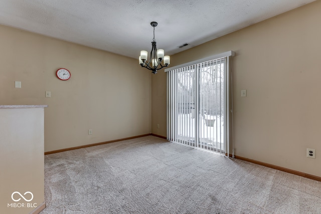 carpeted empty room featuring a notable chandelier and a textured ceiling