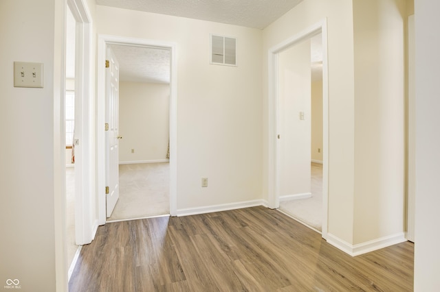 corridor with a textured ceiling and hardwood / wood-style floors