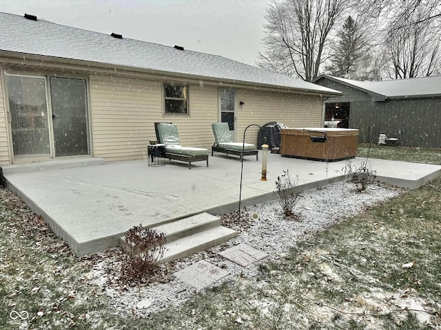 snow covered back of property featuring a patio area and a hot tub