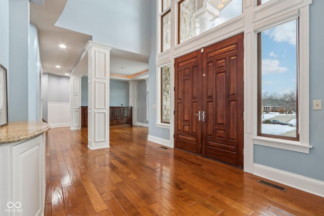 foyer entrance featuring a healthy amount of sunlight, a high ceiling, hardwood / wood-style floors, and ornate columns