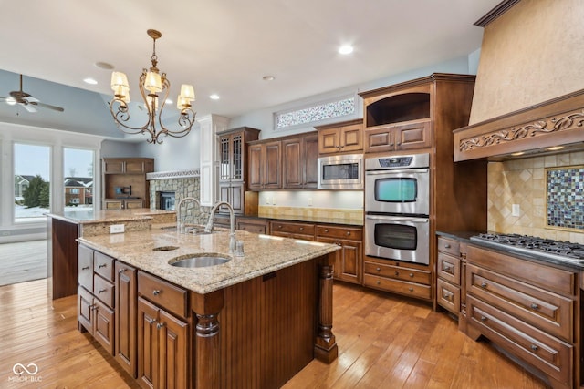 kitchen featuring decorative light fixtures, sink, stainless steel appliances, light stone countertops, and a center island with sink