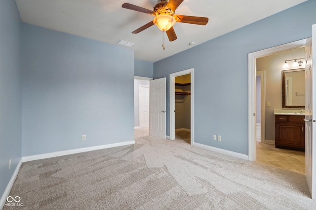 unfurnished bedroom featuring ceiling fan, ensuite bathroom, light carpet, a walk in closet, and a closet