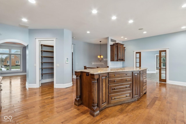 kitchen with decorative light fixtures, a center island, light hardwood / wood-style floors, and light stone countertops