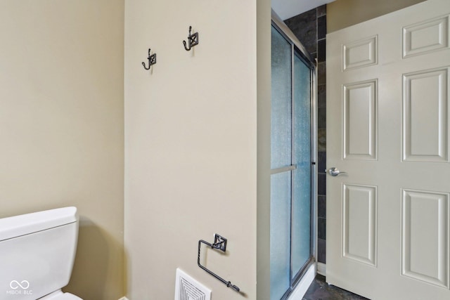 bathroom featuring a shower with door and toilet