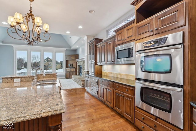 kitchen with lofted ceiling, sink, hanging light fixtures, stainless steel appliances, and light stone counters