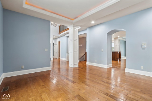 empty room featuring a tray ceiling, crown molding, and light wood-type flooring